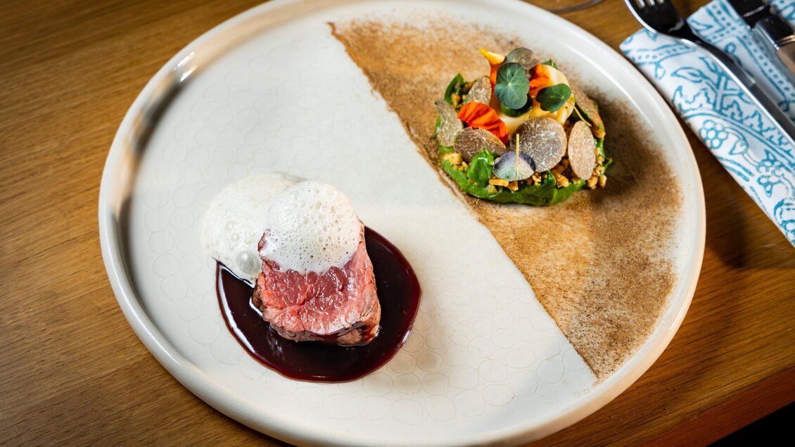 Ein elegant angerichtetes Gericht mit zartem Fleisch und einer feinen Soße. Auf der rechten Seite befindet sich eine Gemüseportion in einer essbaren Schale. | © Graz Tourismus - Werner Krug
