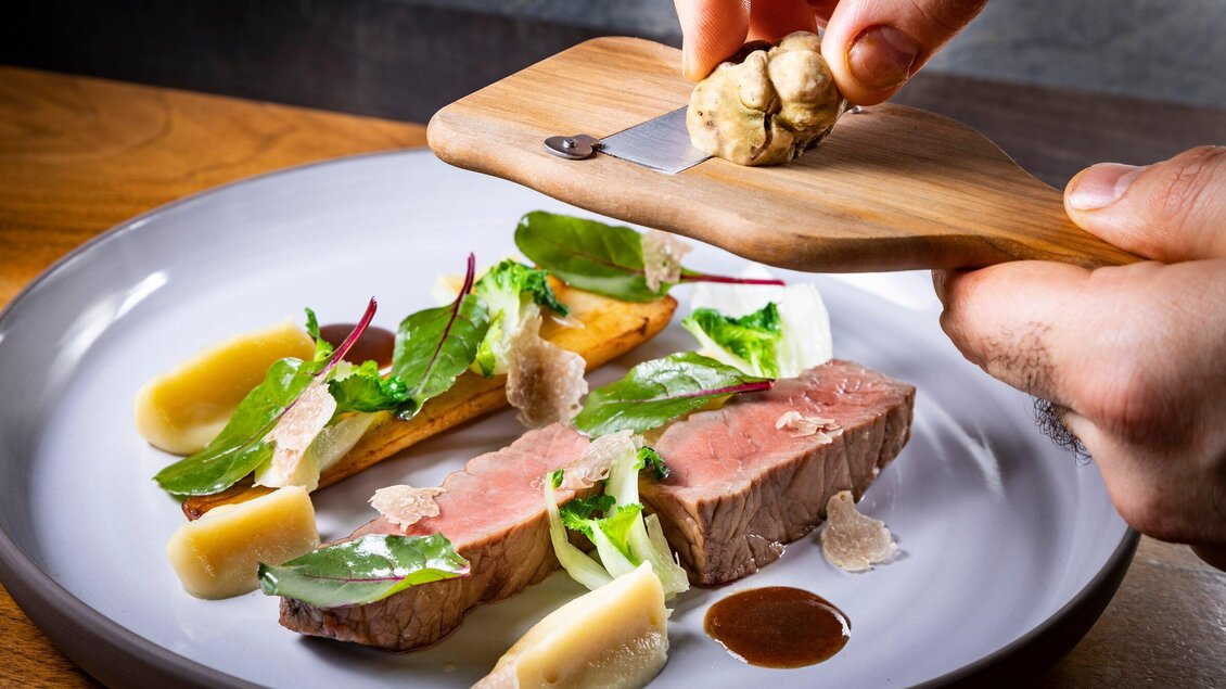 Ein hochwertiges Gericht auf einem Teller, das aus zartem Fleisch, frischen Kräutern und Gemüse besteht. Eine Person reibt gerade eine Trüffel über das Essen. | © Graz Tourismus - Werner Krug