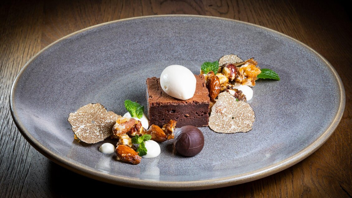 Ein elegantes Dessert auf einem grauen Teller. Es besteht aus Schokoladenkuchen, einer Kugel Eis, dekorativen Nüssen und Minzblättern. | © Graz Tourismus - Werner Krug