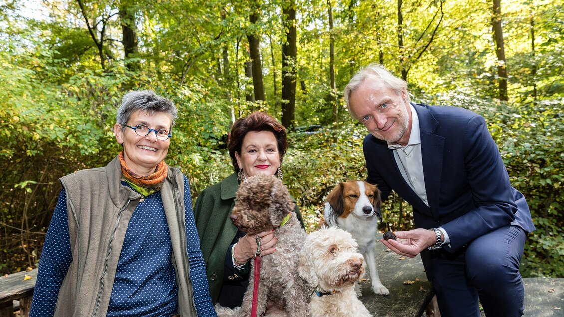 Drei Personen stehen im Wald und posieren lächelnd mit vier Hunden. Die Bäume sind grün und die Atmosphäre ist freundlich und entspannt. | © Graz Tourismus - Harry Schiffer