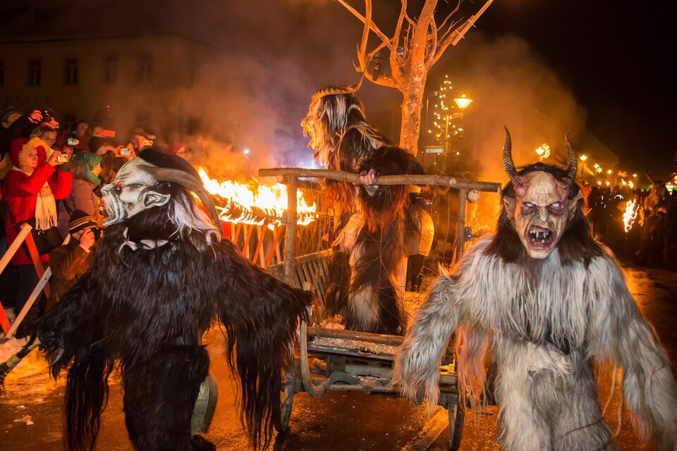 Eine Parade mit verkleideten Menschen in schaurigen Kostümen und Masken. Im Hintergrund brennen Fackeln und eine Menschenmenge beobachtet das Spektakel. | © Fred Lindmoser