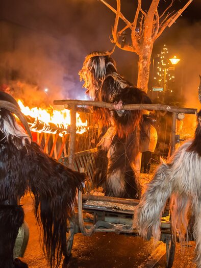 Eine Parade mit verkleideten Menschen in schaurigen Kostümen und Masken. Im Hintergrund brennen Fackeln und eine Menschenmenge beobachtet das Spektakel. | © Fred Lindmoser