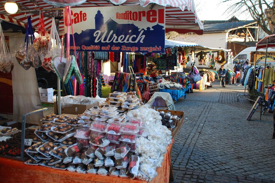 Ein lebhafter Markt mit verschiedenen Ständen und Waren. Es gibt süße Leckereien und bunte Kleidung zu sehen. | © ©Thermen-&Vulkanland/Lederer Josef
