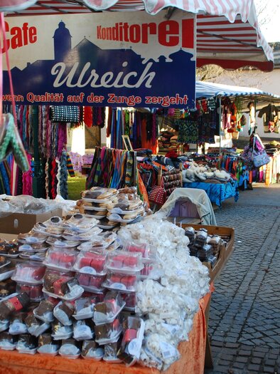 A lively market with various stalls and goods. There are sweet treats and colorful clothing to see. | © ©Thermen-&Vulkanland/Lederer Josef