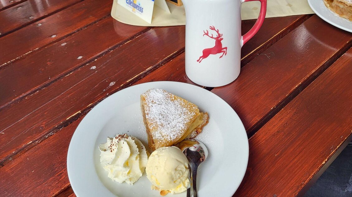 Ein Teller mit einem Stück Kuchen, Sahne und einer Kugel Eis. Dazu steht eine Kanne mit einem Rentier-Motiv. | © Petra Kirchschlager