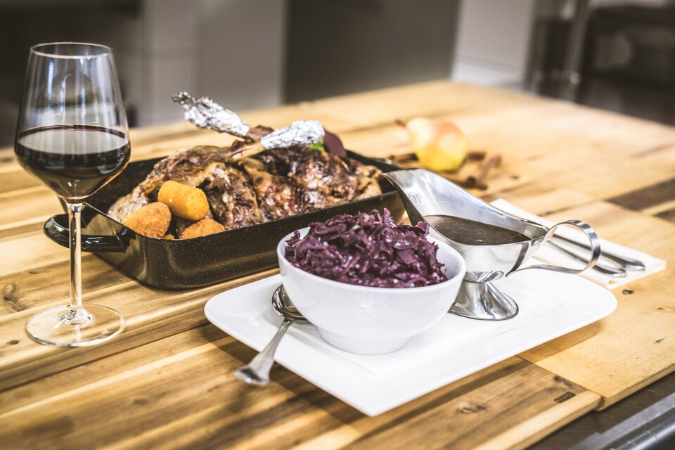 Ein elegantes Gericht mit gebratenem Fleisch, Kartoffeln und Rotkohl. Dazu ein Glas Rotwein auf einem Holztisch. | © Christina Schoberleitner