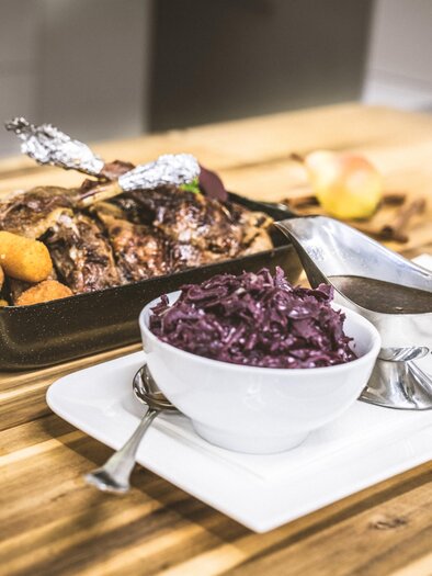 Ein elegantes Gericht mit gebratenem Fleisch, Kartoffeln und Rotkohl. Dazu ein Glas Rotwein auf einem Holztisch. | © Christina Schoberleitner