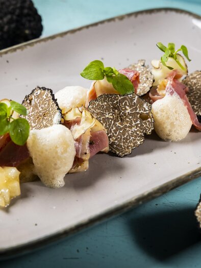 An elegant dish with truffles, ham, and various sides on a plate. The presentation is appealing and modern. | © Graz Tourismus - Werner Krug