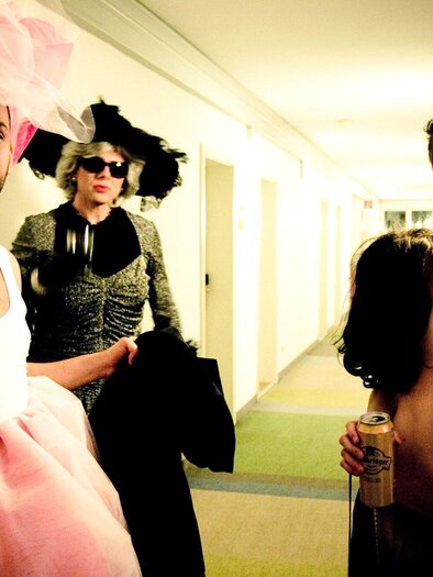 Three people in unusual costumes are standing in a hallway. Two of them are holding drinks in their hands. | © Alexandra Thompson