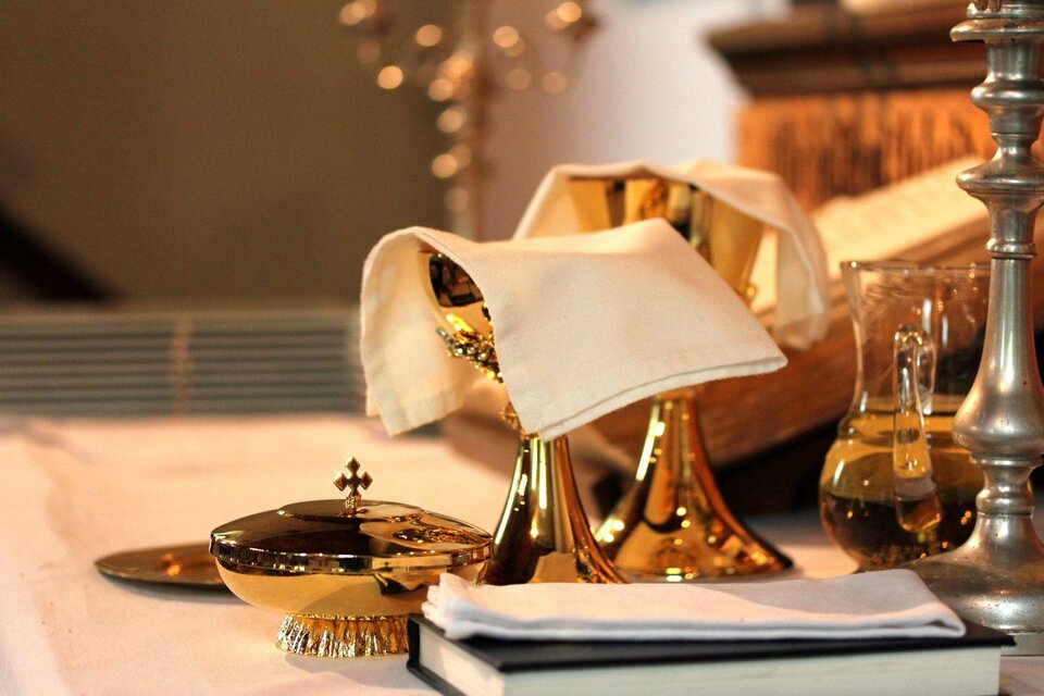 Ein Tisch mit goldenen Kelchen und einem Kreuz. Daneben stehen eine Glasflasche und ein aufgeschlagenes Buch. | © Tieber Doris