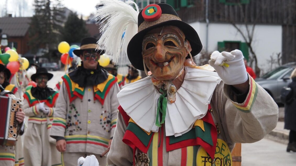 Die Gruppe der Altausseer Knopferl in ihren traditionellen Kostümen und Masken feiert ihren Paradiestag während des Faschingstreiben im Ausseerland. Sie tragen ein weißes Gewand mit bunten Verzierungen und einem Hut, und halten bunte Luftballons in ihren mit weißen Handschuhen verdeckten Händen. Sie ziehen durch die Straßen von Altaussee und sorgen für festliche Stimmung. | © Theresa Schwaiger