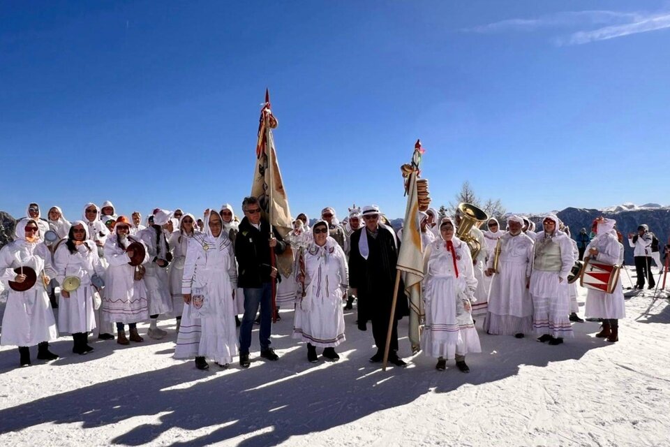 Die Gruppe der Altausseer Trommelweiber in Aufstellung zu ihrem jährlichen Umzug während des Ausseer Faschings. Sie tragen die traditionelle Verkleidung, bestehend aus weißen Nachtgewändern, Schlafhauben und Masken. Sie stehen auf schneebedecktem Boden in Altaussee unter einem strahlend blauen Himmel, und halten Fahnen, Trommeln und Trompeten in ihren Händen. | © Martina Gaisberger