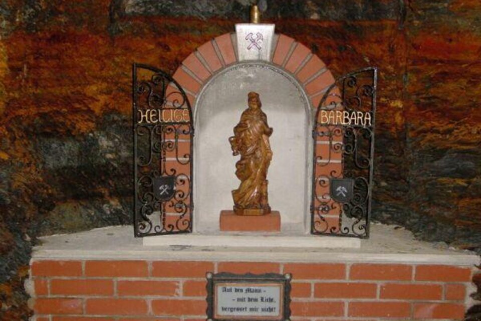 Eine Statue der heiligen Barbara ist in einer Nische mit einem dekorativen Gitter untergebracht. Der Raum hat eine rustikale Steinmauer und eine bescheidene, aber ehrwürdige Atmosphäre. | © Bergbauverein Öblarn