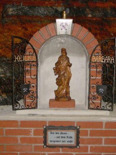 Eine Statue der heiligen Barbara ist in einer Nische mit einem dekorativen Gitter untergebracht. Der Raum hat eine rustikale Steinmauer und eine bescheidene, aber ehrwürdige Atmosphäre. | © Bergbauverein Öblarn