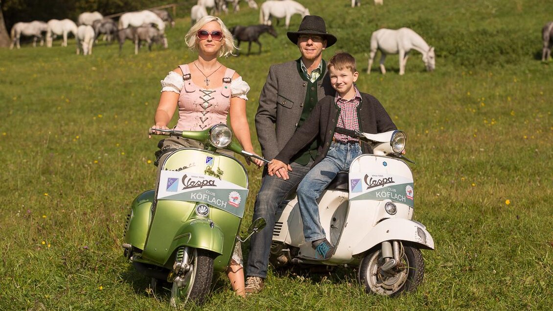 Familie in Tracht auf Vespas vor Lipizzanern auf der Weide im Lipizzanergestüt Piber in Köflach. | © VideoFotograf.at