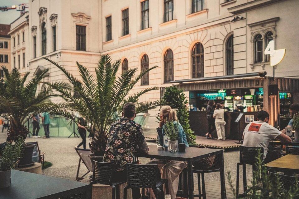 Ein lebhaftes café im Freien mit Palmen und Tischen. Menschen genießen die Atmosphäre in einer städtischen Umgebung. | © CIS
