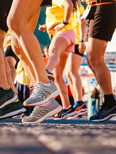 Eine Gruppe von Läufern in Sportkleidung bewegt sich in einem Wettlauf. Die Füße sind in bunten Turnschuhen zu sehen, während sie über die Straße laufen. | ©  Pexels