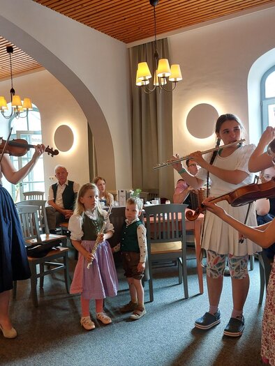 Eine kleine Gruppe von Mädchen spielt in einem Restaurant Geige. Im Hintergrund sitzen weitere Gäste und beobachten die Aufführung. | © Alfred Edegger