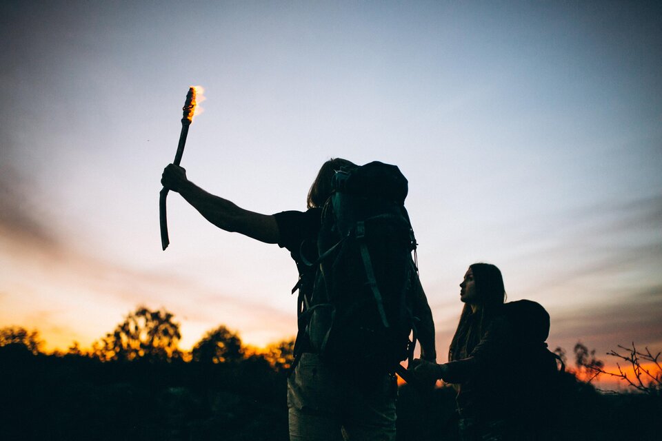 Zwei Personen mit Rucksäcken stehen im Freien bei Sonnenuntergang. Eine Person hält eine brennende Fackel in die Höhe. | © Gemeinde Floing
