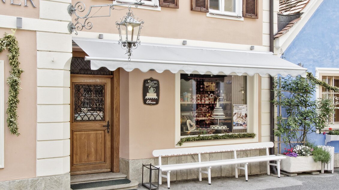 Ein charmantes Geschäft mit einem Holzportal und einer großen Fensterfront. Die Fassade ist in sanften Farbtönen gehalten und bietet eine einladende Atmosphäre.