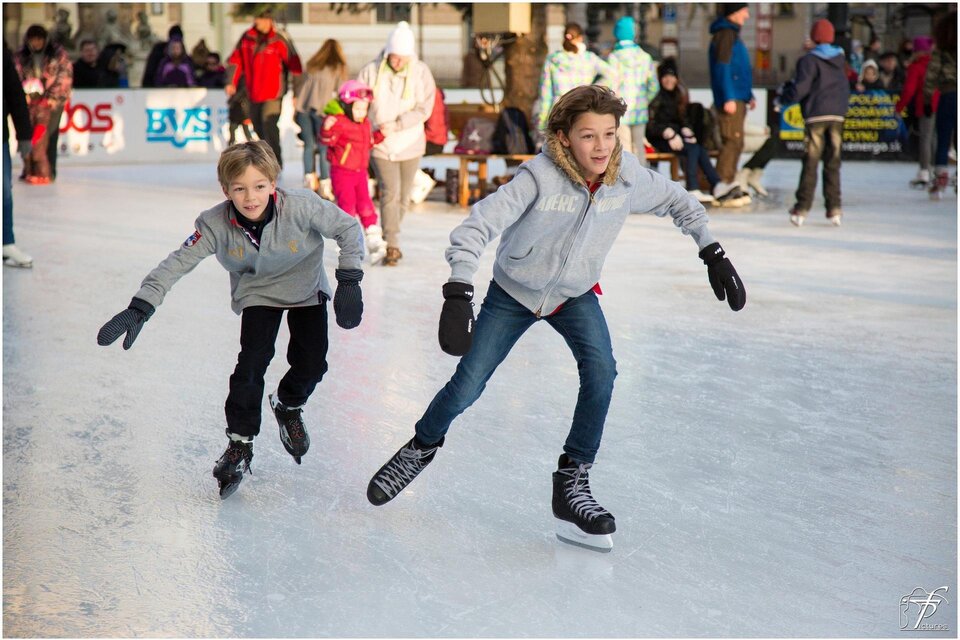 Zwei Kinder laufen fröhlich auf der Eisbahn. Im Hintergrund sind weitere Schlittschuhläufer und Zuschauer zu sehen. | © Pixabay.com