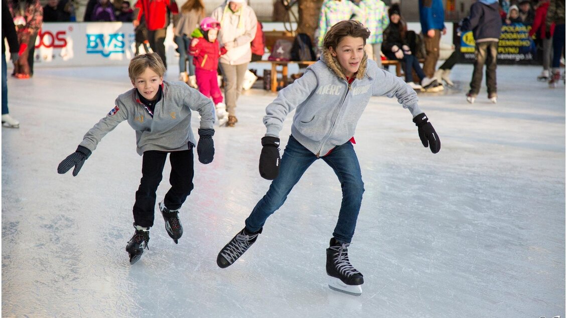 Zwei Kinder laufen fröhlich auf der Eisbahn. Im Hintergrund sind weitere Schlittschuhläufer und Zuschauer zu sehen. | © Pixabay.com
