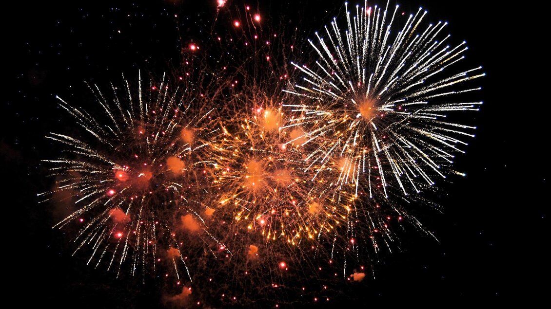 Ein strahlendes Feuerwerk mit bunten Lichtblitzen gegen den Nachthimmel. Die Farben leuchten in Rot, Orange und Weiß. | © pixabay.com