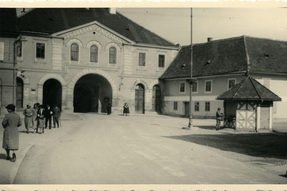Historische Schwarz-Weiß-Aufnahme des Stadttors in Fürstenfeld, Steiermark, mit Passanten in zeittypischer Kleidung, markanten Torbögen und angrenzenden Gebäuden – Einblick in das frühere Stadtleben und kulturelles Erbe der Erlebnisregion Thermen- & Vulkanland. | © Museum Pfeilburg