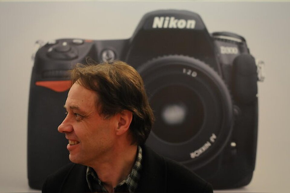 Vortragender Rainer Fuchs im Seitenprofil vor einer großformatigen Abbildung einer Nikon-Kamera.  | © Rainer Fuchs