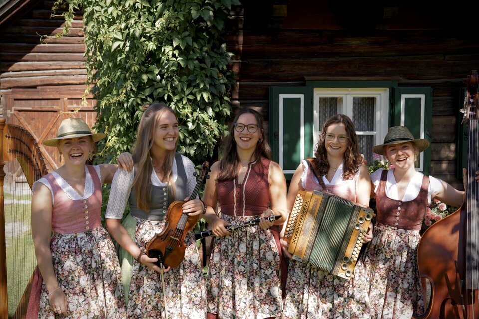 Eine Gruppe von Menschen in traditioneller Kleidung steht in einem gemütlichen Raum. Im Hintergrund sind dekorative Elemente und Jagdtrophäen sichtbar. | © Kohlröserl Dirndln