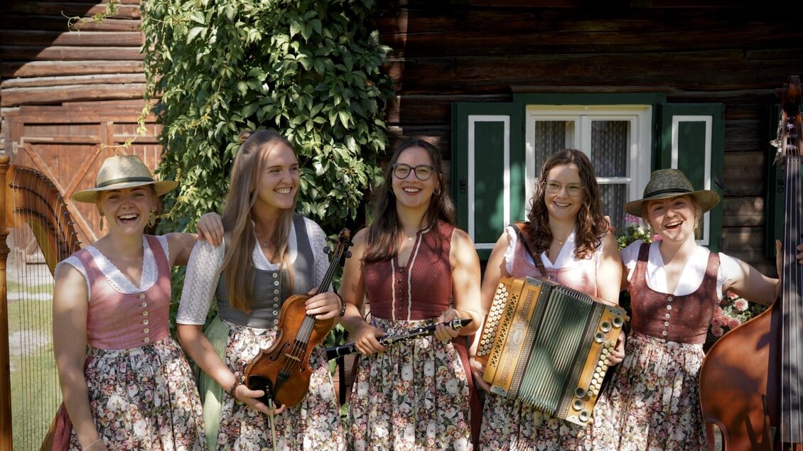 Eine Gruppe von Menschen in traditioneller Kleidung steht in einem gemütlichen Raum. Im Hintergrund sind dekorative Elemente und Jagdtrophäen sichtbar. | © Kohlröserl Dirndln
