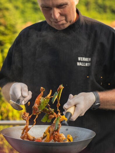 Ein Koch bereitet ein Gericht im Wok zu. Frisches Gemüse und Fleisch werden in der Pfanne geschwenkt. | © Vulkanlandhotel Legenstein