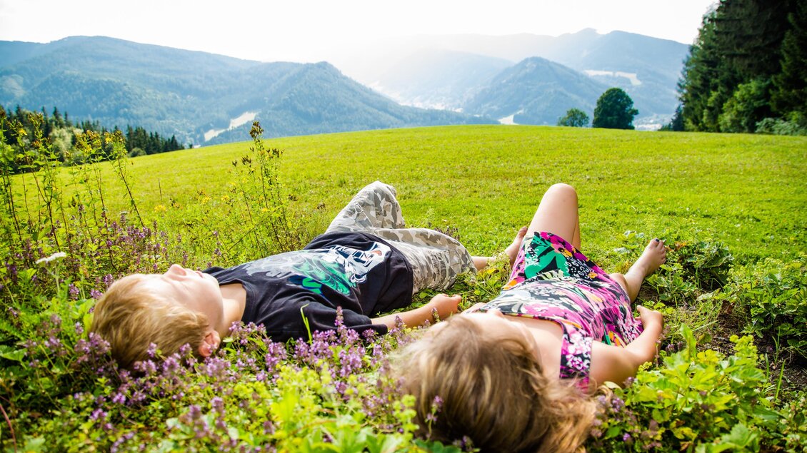 2 entspannte Kids die die Seele im grünen Gras am Waldesrand baumeln lassen | © nicolseiser.at