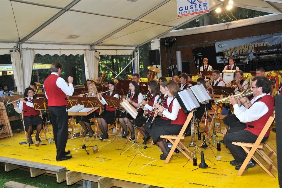 Ein Blasorchester spielt unter einem Zelt. Die Musiker tragen rote Westen und genießen die Darbietung. | © Walfest_Archiv TVB