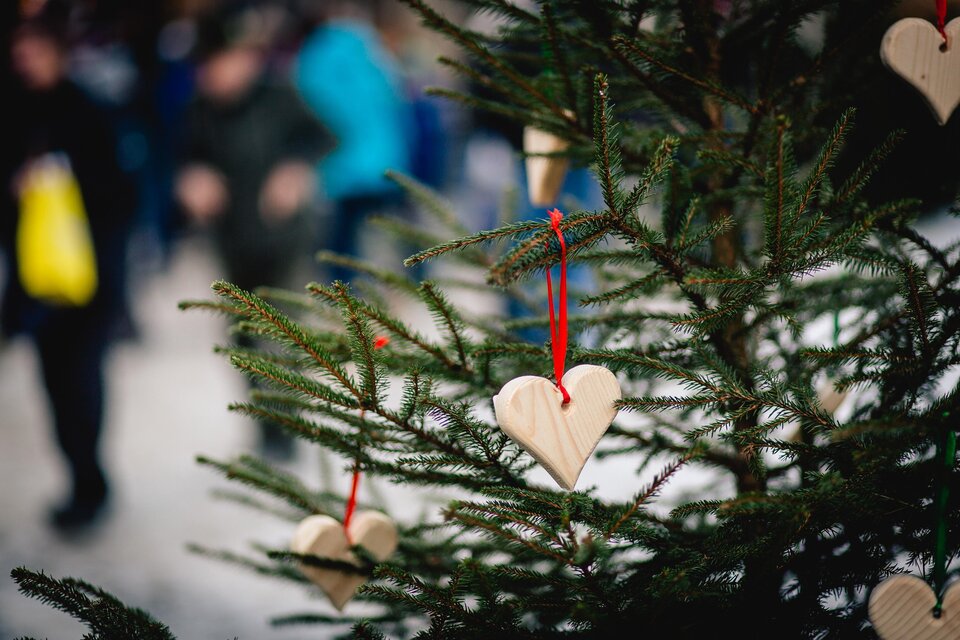 Ein mit Holzherzen geschmückter Weihnachtsbaum steht im Vordergrund. Im Hintergrund sind unscharfe Menschen zu sehen, die sich bewegen. | © TV Hochsteiermark, nicoleseiser.at