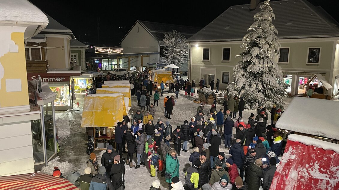 Ein belebter Weihnachtsmarkt bei Nacht, umgeben von Schnee. Viele Menschen genießen die festliche Atmosphäre und die bunten Stände. | © Marktgemeinde Krieglach