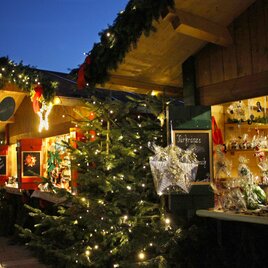A festive Christmas market with illuminated stalls and a decorated Christmas tree. The atmosphere is charming and inviting. | © A. Pech