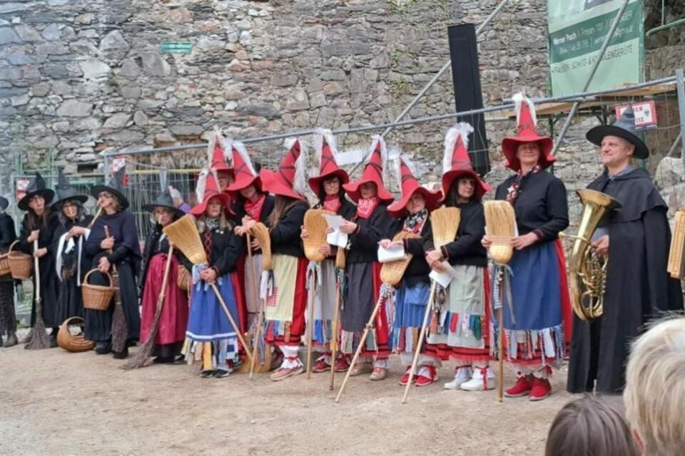 Eine Gruppe von Menschen in traditionellen Kostümen steht vor einer alten Steinmauer. Sie tragen rote Hüte und halten verschiedene Utensilien. | © Erich Brandl