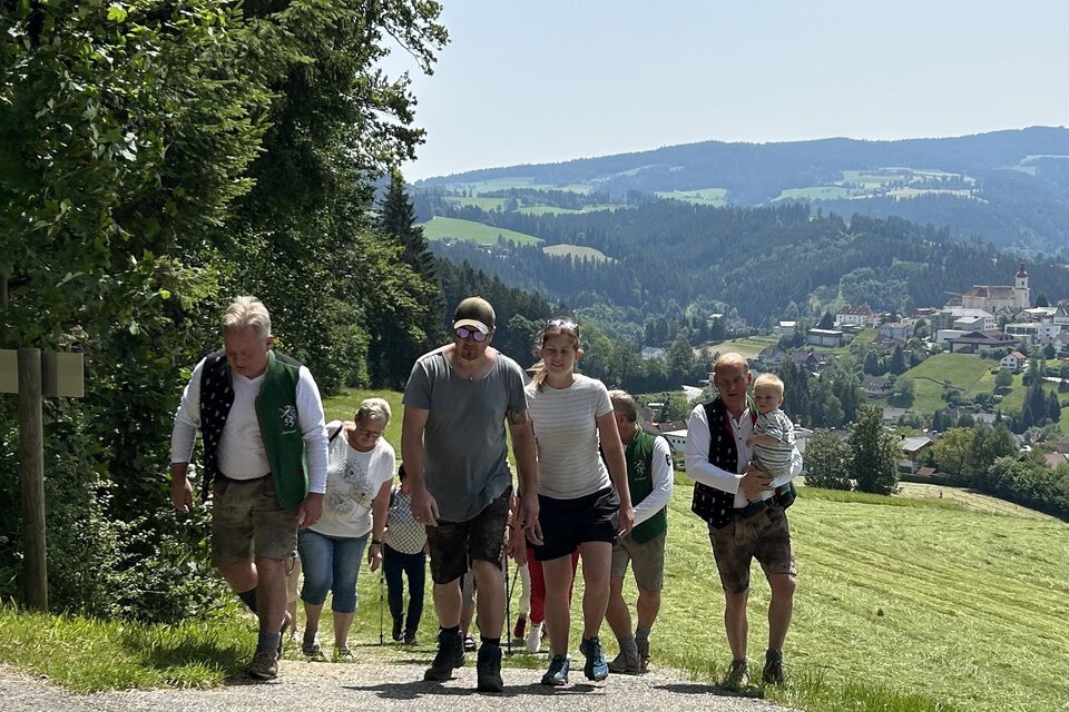 Eine Gruppe von Menschen wandert einen malerischen Weg entlang, umgeben von grünen Feldern und hügeliger Landschaft. Im Hintergrund ist eine kleine Stadt sichtbar. | © EDL-Event GmbH