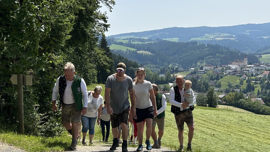 Eine Gruppe von Menschen wandert einen malerischen Weg entlang, umgeben von grünen Feldern und hügeliger Landschaft. Im Hintergrund ist eine kleine Stadt sichtbar. | © EDL-Event GmbH