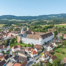 Eine malerische Stadt mit historischen Gebäuden und grünen Landschaften. Im Hintergrund erheben sich sanfte Hügel unter einem klaren Himmel.