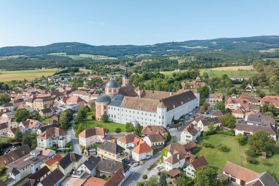 Eine malerische Stadt mit historischen Gebäuden und grünen Landschaften. Im Hintergrund erheben sich sanfte Hügel unter einem klaren Himmel.