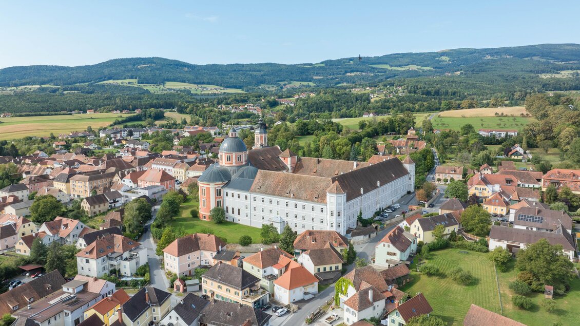 Eine malerische Stadt mit historischen Gebäuden und grünen Landschaften. Im Hintergrund erheben sich sanfte Hügel unter einem klaren Himmel.