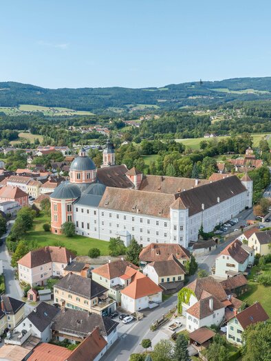 Eine malerische Stadt mit historischen Gebäuden und grünen Landschaften. Im Hintergrund erheben sich sanfte Hügel unter einem klaren Himmel.