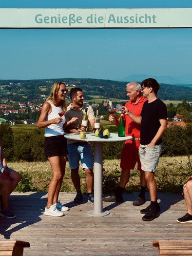 Eine fröhliche Gruppe von Menschen versammelt sich an einem Aussichtspunkt. Sie genießen Getränke und die schöne Aussicht auf die Landschaft. | © Gemeinde BW