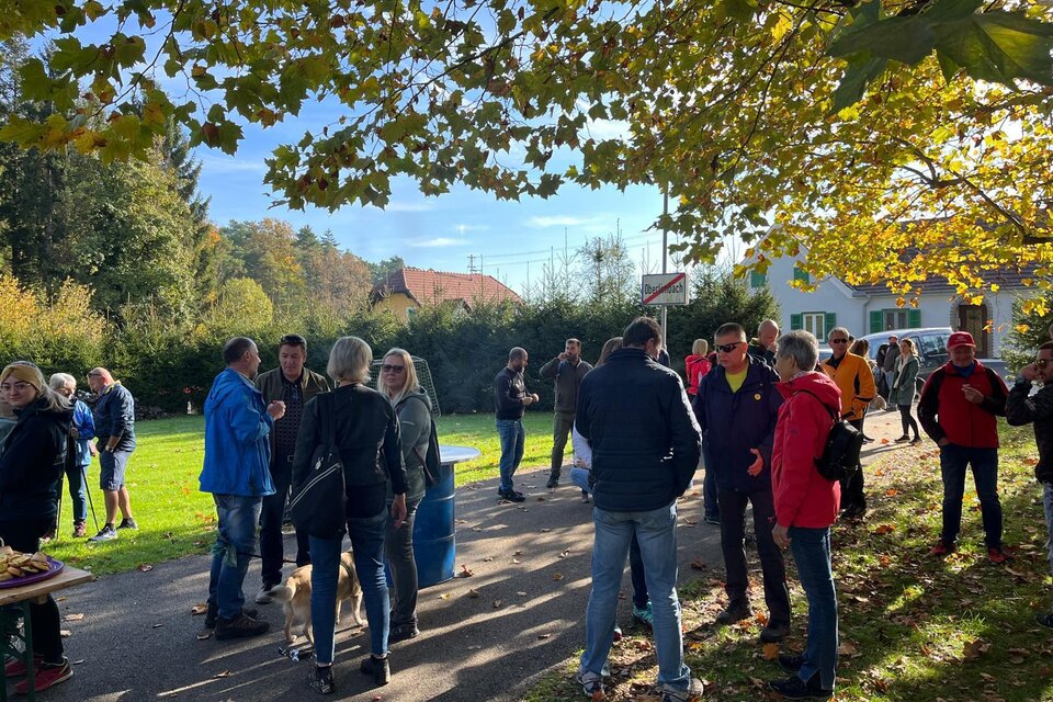 Eine Gruppe von Menschen steht im Freien unter einem Baum mit bunten Blätter. Es scheint einen geselligen Austausch zwischen den Teilnehmern zu geben. | © Mild