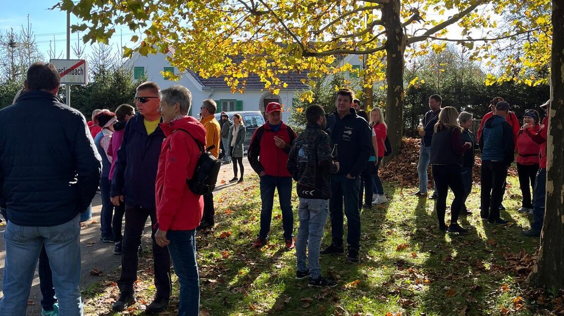 Eine Gruppe von Menschen steht unter Bäumen mit herbstlichen Blättern. Die Sonne scheint, und die Stimmung wirkt entspannt. | © Mild