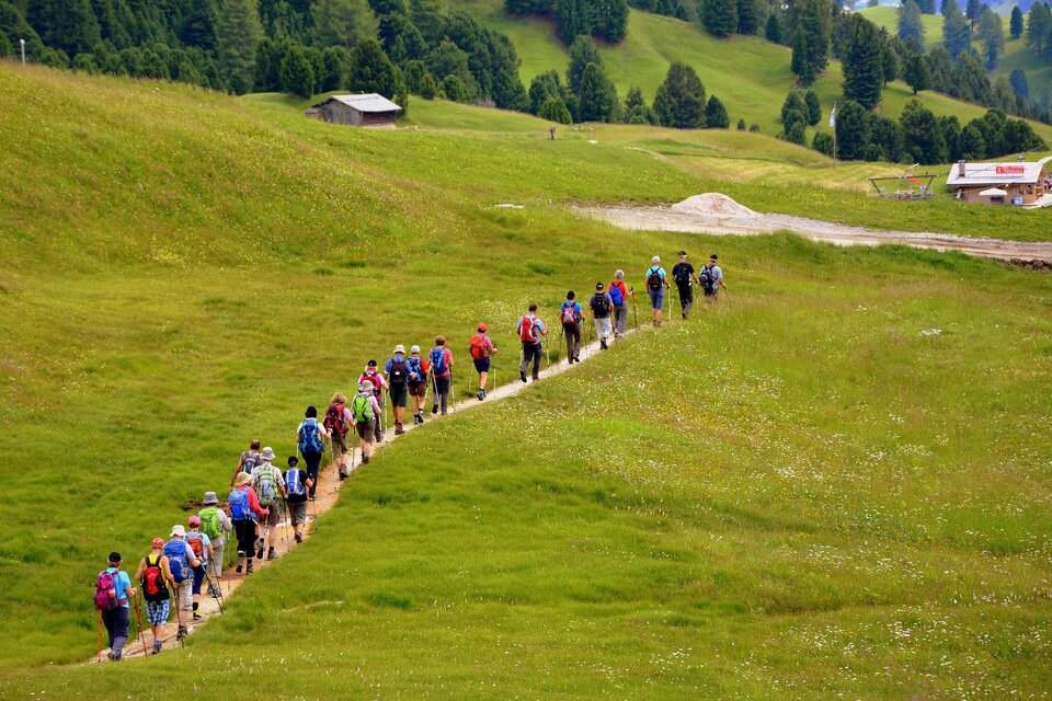 Ein Wanderer mit einem Rucksack geht auf einem Weg durch eine grüne Landschaft. Im Hintergrund sind sanfte Hügel und Bäume zu sehen. | © Pixabay
