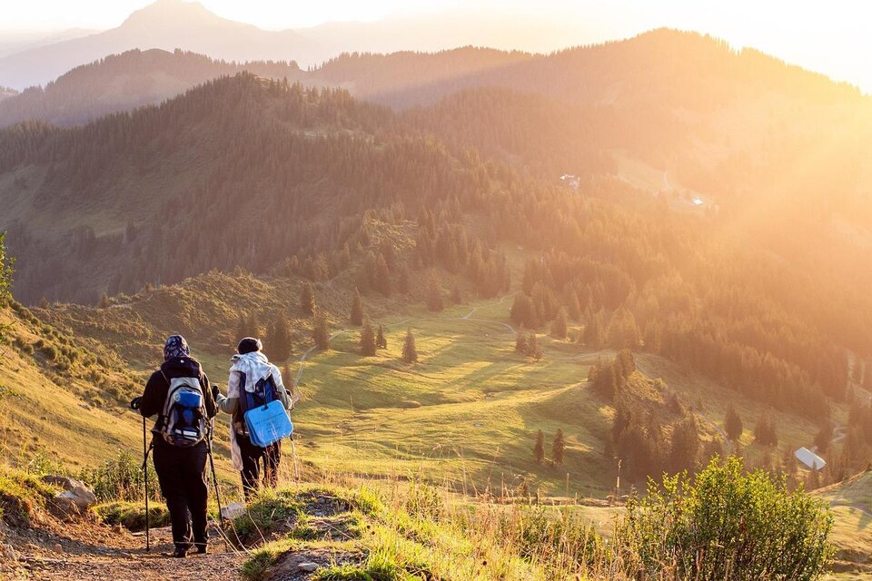 Zwei Wanderer gehen auf einem Pfad durch eine bergige Landschaft. Die Sonne scheint und sorgt für eine goldene Beleuchtung der Umgebung. | © pixabay.com