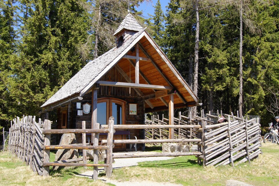 Holzkapelle am Reinischkogel in der Weststeiermark, umgeben von Wald und Holzzaun, sonniger Ausflugsort in der Natur. | © andikohlbacher